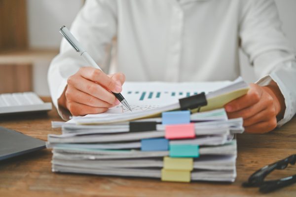 a person is writing on a stack of papers with a pen