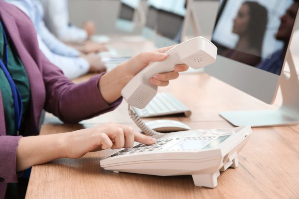 technical support operator dialing number on telephone at table, closeup